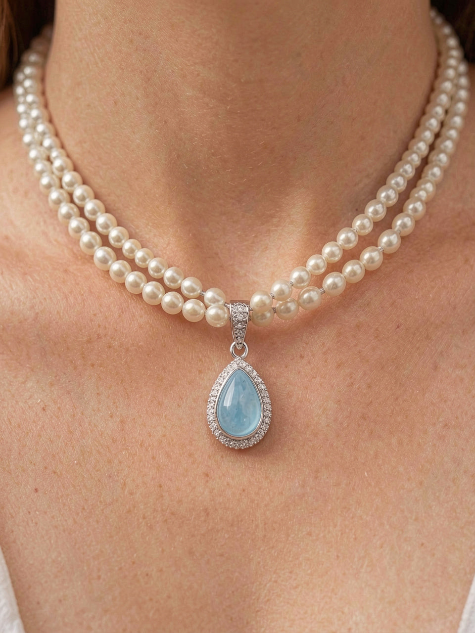 Detalle macro del collar de perlas de dos hilos en capas con dije en forma de gota de piedra azul cabujón y halo de pavé, sin artefactos flotantes